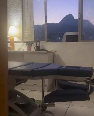 Sala de atendimento com maca e, pela janela, o Cristo Redentor ao entardecer